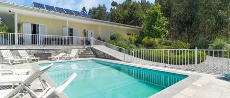 A swimming pool with lounge chairs, a white fence, and solar panels on the building.