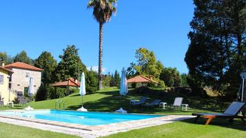 Un área de piscina con cielo azul despejado, una palmera y un edificio con techo rojo.