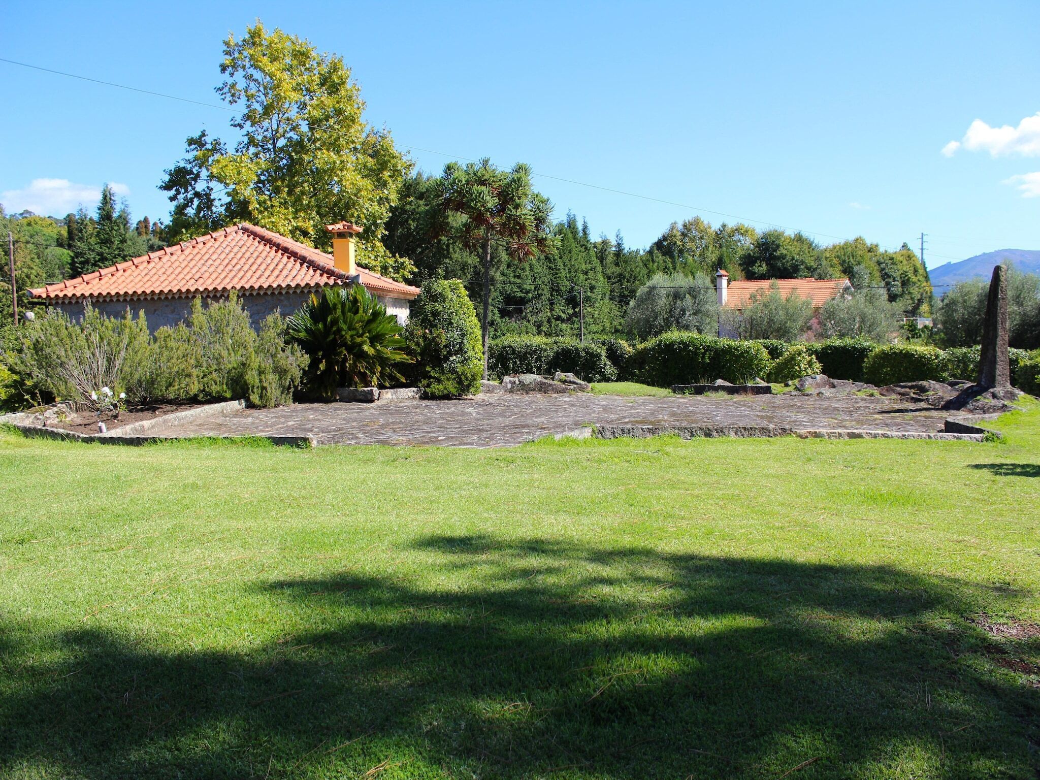 A house with a tiled roof, surrounded by a well-maintained lawn and various shrubs.