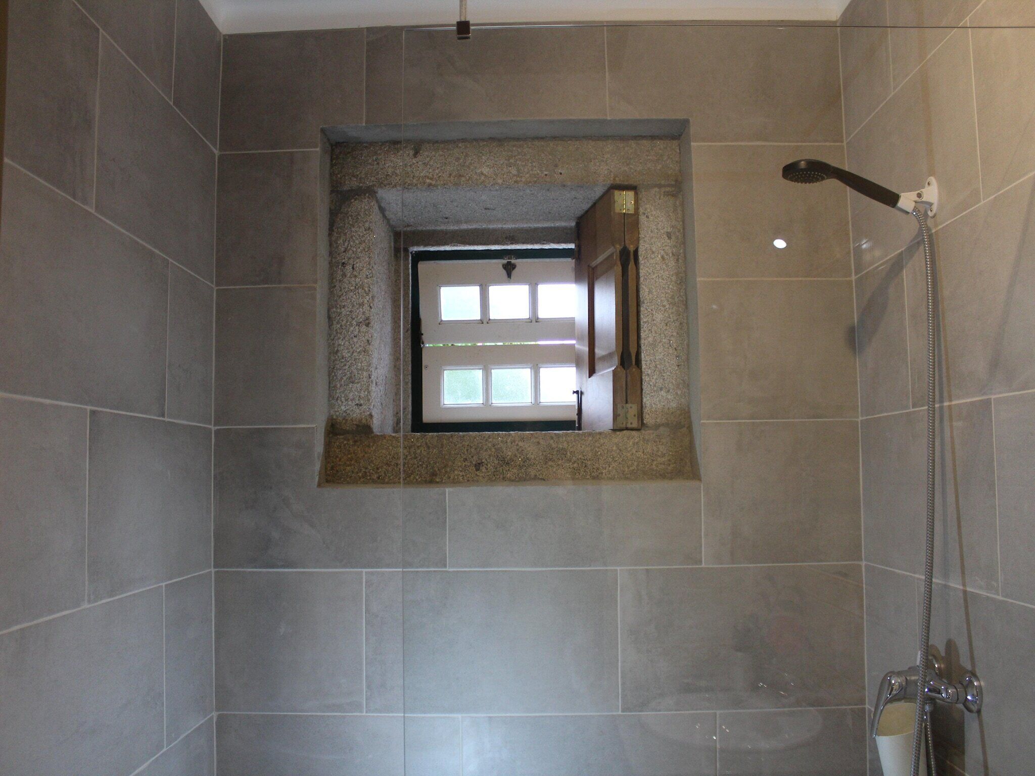 Un baño con ducha, ventana y pared de azulejos.
