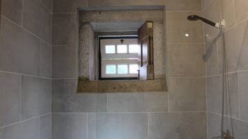 Un baño con ducha, ventana y pared de azulejos.