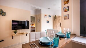 A modern kitchen with a wooden countertop, blue plates, and glasses. There is a TV mounted on the wall and a dining area with a white sofa. - Slava by Sevilla Luxury Suite (Sevilla)