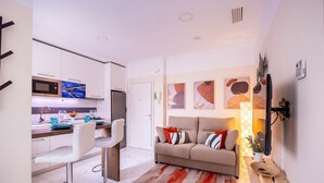 A modern kitchen with white cabinets, a microwave, and a refrigerator. There is a dining area with a white sofa and a red and white striped rug. - Slava by Sevilla Luxury Suite (Sevilla)