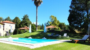 A swimming pool with lounge chairs, a palm tree, and a stone building. - Santa Comba Garden Cottage (Ponte de Lima)