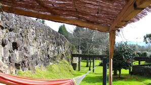 A hammock under a wooden pergola, a stone wall, and a grassy garden with flowers. - Santa Comba Garden Cottage (Ponte de Lima)