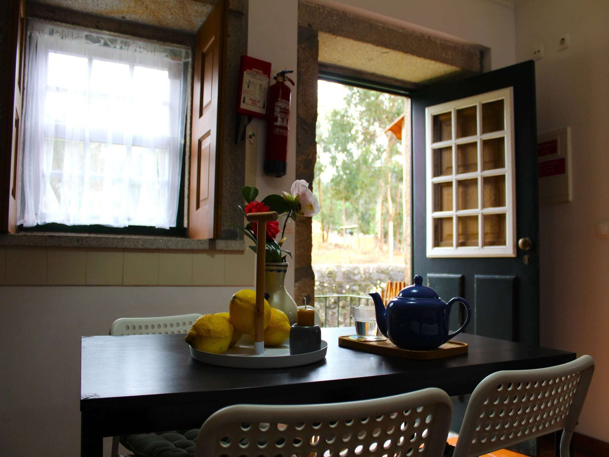 Un comedor con una mesa dispuesta para dos, un florero con flores, limones y una tetera.