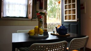 A dining area with a table set for two, a vase with flowers, lemons, and a teapot. - Santa Comba Garden Cottage (Ponte de Lima)