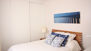 Un letto rifatto con un poggiatesta in legno, una lampada da comodino e un quadro raffigurante un molo.