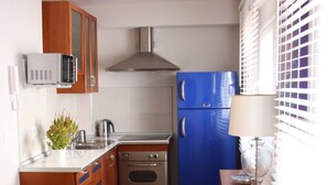 Una cucina compatta con mobili in legno, un forno in acciaio inossidabile, un frigorifero blu e un piccolo tavolo con oggetti decorativi.