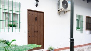 Een wit gebouw met een houten deur, een raam met groene roede en een airconditioning.