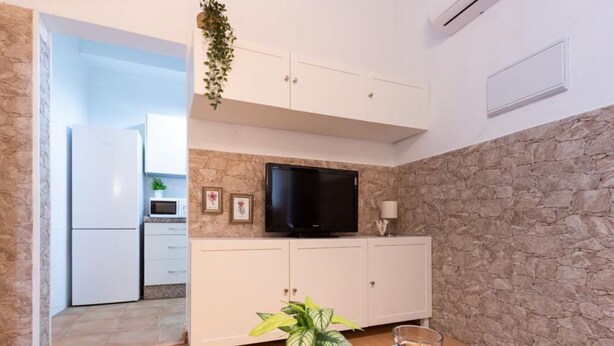 Een compacte wooneenheid met een kitchenette, een flatscreen televisie, een accentmuur van steen en een eethoek met een tafel gedekt voor twee personen.