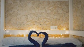 Een bed met een stenen muur erachter, een wit hoofdeinde en een decoratie in de vorm van een hart, gemaakt van dekens.