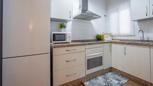 Een moderne keuken met witte kastjes, een Bosch koelkast, een magnetron en een fornuis.