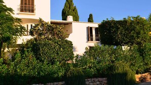 Un edificio blanco con un muro de piedra y un árbol alto al frente.