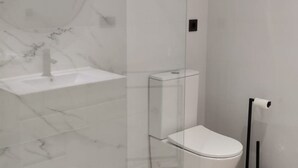 Et moderne badeværelse med vask, toilet og brusekabine i glas.