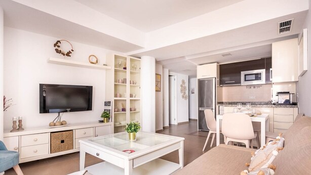Un salon moderne avec un téléviseur à écran plat, une table basse en verre et un canapé. Il y a également un coin cuisine équipé d’un four à micro-ondes et d’un réfrigérateur.