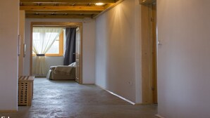 A narrow hallway with wooden beams on the ceiling, a window with sheer curtains, and a door at the end.