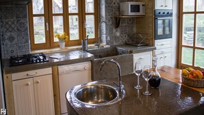 A kitchen with a stainless steel sink, a microwave, an oven, and a dishwasher. There are windows with wooden frames and a view of the outdoors.