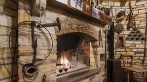 Ein Steinkamin mit Feuer, ein Holzstuhl sowie verschiedene Werkzeuge und Dekorationen an der Wand.