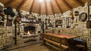 Ein rustikaler Raum mit Steinwänden, Holzboden und einem Kamin aus Stein. Dazu ein Holztisch und Bänke.