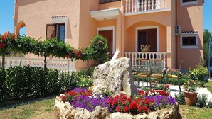 A two-story building with a balcony, surrounded by colorful flowers and a decorative fence. - Apartment in Vrsi near the Sea (Vrsi-Mulo)