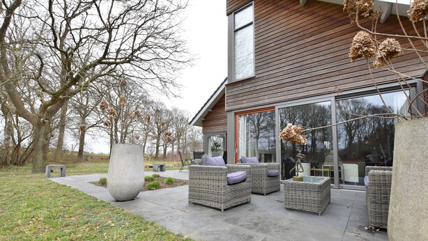 Una casa moderna con patio arredato con mobili in vimini e un grande vaso.
