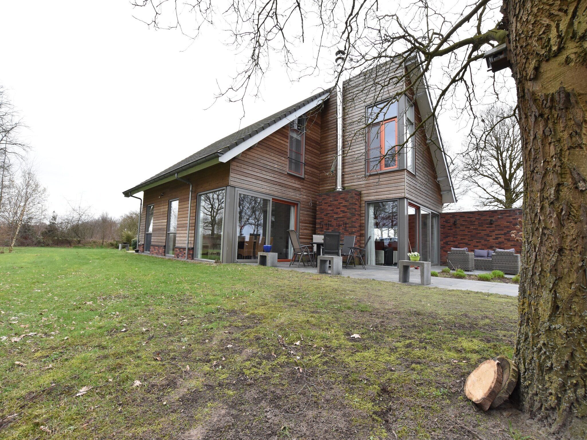 Een modern huis met een schuin dak, grote ramen en een patio met buitenmeubilair.