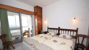 A bedroom with two beds, a window with a view, a wooden headboard, and a nightstand.