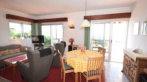 A living room with a sofa, chairs, a table, a TV, and a balcony with a view.