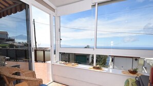 A balcony with wicker furniture, a table with a blue tablecloth, and a view of the sea.