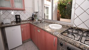 A compact kitchen with a dishwasher, a gas stove, and a window with a view of a garden.