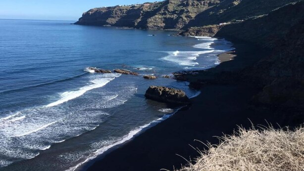 A coastal landscape with a rocky cliff, a beach, and the ocean.