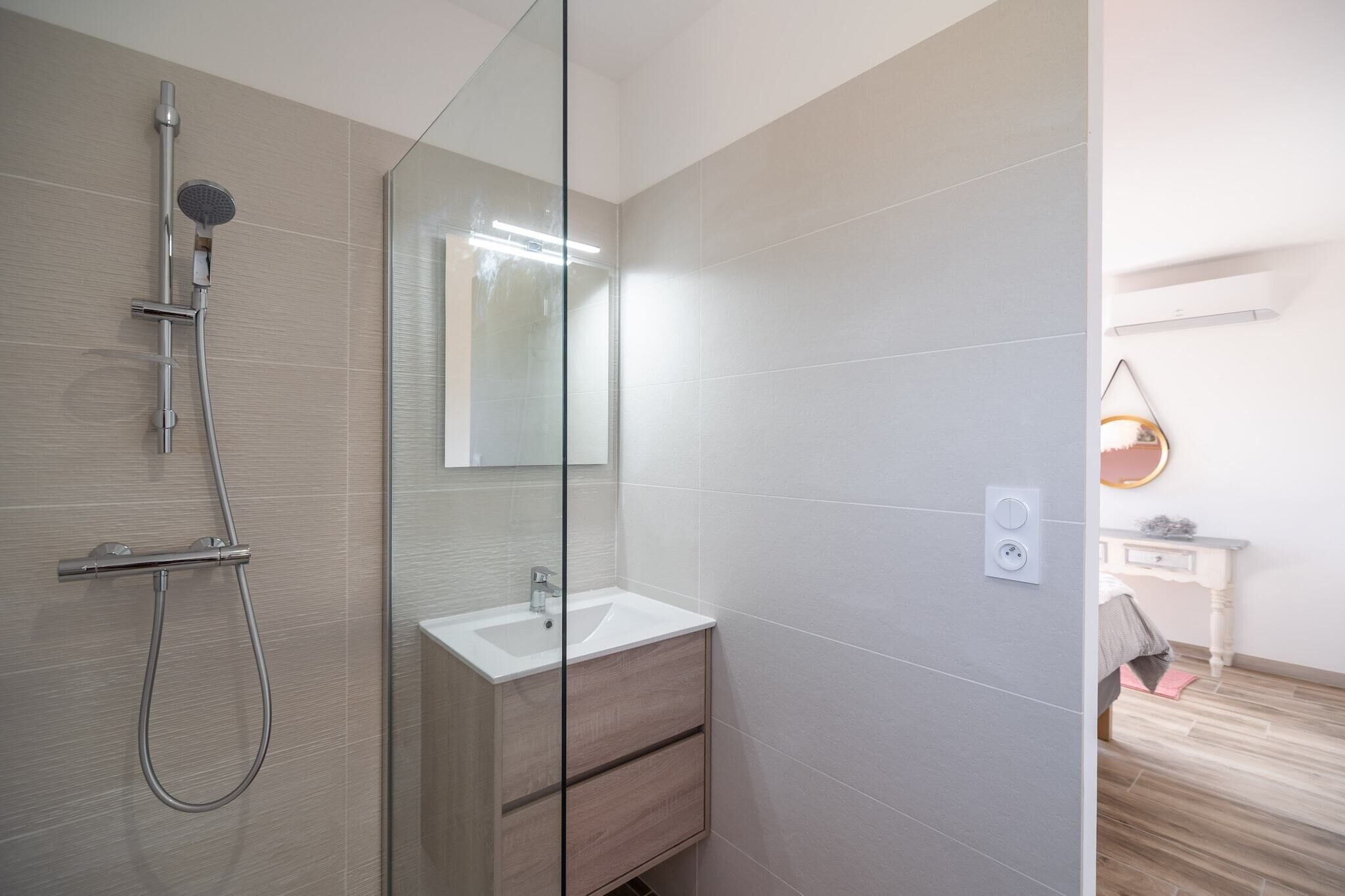 A modern bathroom with a glass shower enclosure, a white sink, and a wooden vanity.