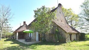 A rustic stone house with a thatched roof, a small patio with a table and chairs, and a green umbrella. - Holiday Home in Decize near Beach (Decize)