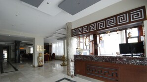 A spacious lobby with a marble reception desk, large windows, and a decorative column. - Hitit Otel (Ankara)