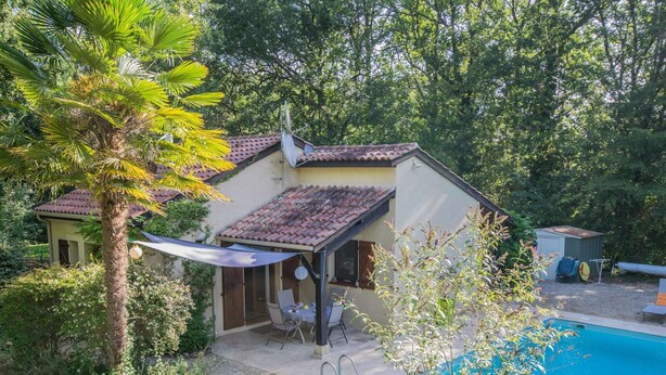 Une maison avec une piscine, entourée d’une végétation luxuriante et dotée d’un patio avec des meubles pour se détendre en plein air.