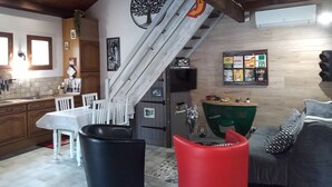 Une cuisine avec un coin repas, un escalier et un salon comprenant un canapé et un fauteuil vert.
