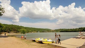 Une jetée au bord du lac, avec des bateaux jaunes, une plage de sable et, en arrière-plan, une colline boisée.