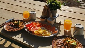 Una mesa de madera con platos de desayuno, una tienda de campaña y vistas a un campo.