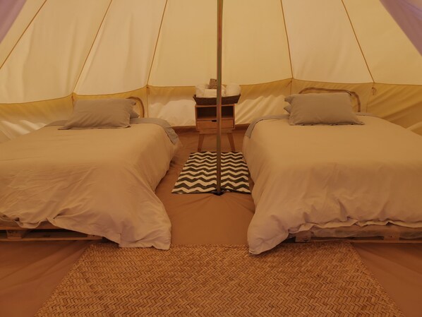 A tent with two beds, each with pillows and a small bedside table.