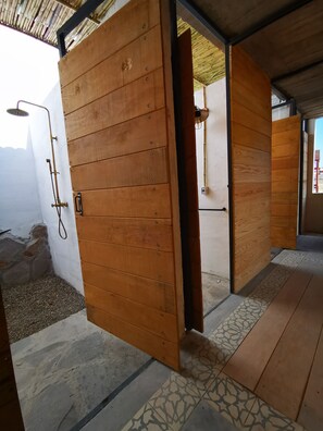 A wooden door with a towel rack and a showerhead, leading to a room with patterned tiles and a concrete floor.