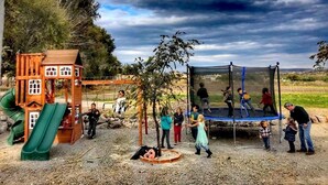 Un parque infantil con una casita de madera, un tobogán y un trampolín.