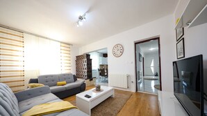 A modern living room with a grey sofa, a coffee table, and a TV. There is a wooden floor, a radiator, and a clock on the wall. - Holiday Home in Policnik with Private Pool (Policnik)