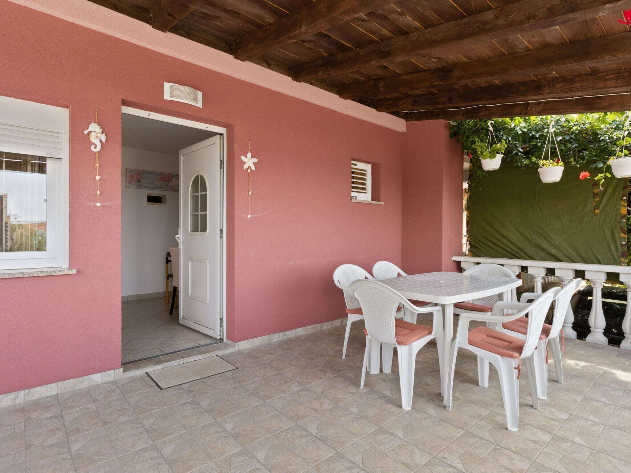 A covered patio with a table and chairs, a wooden ceiling, and a door leading to an interior space.