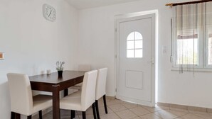 Un coin repas avec une table en bois et quatre chaises, une horloge au mur et une porte avec une fenêtre.