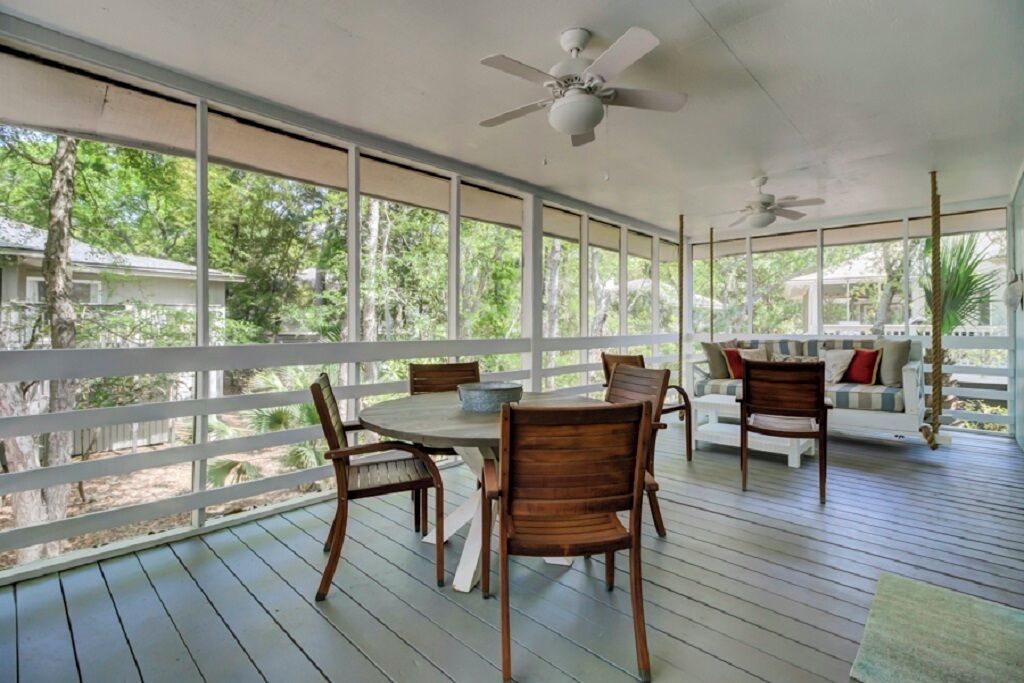 Un espace extérieur abrité, doté d’une terrasse en bois, d’une table ronde avec des chaises et d’un canapé avec des coussins.