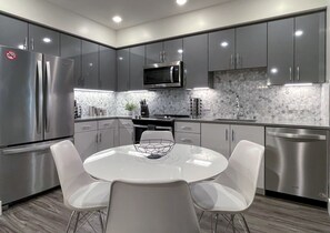 A modern kitchen with stainless steel appliances, a microwave, and a dishwasher. There is a round table with four chairs and a decorative bowl on it.