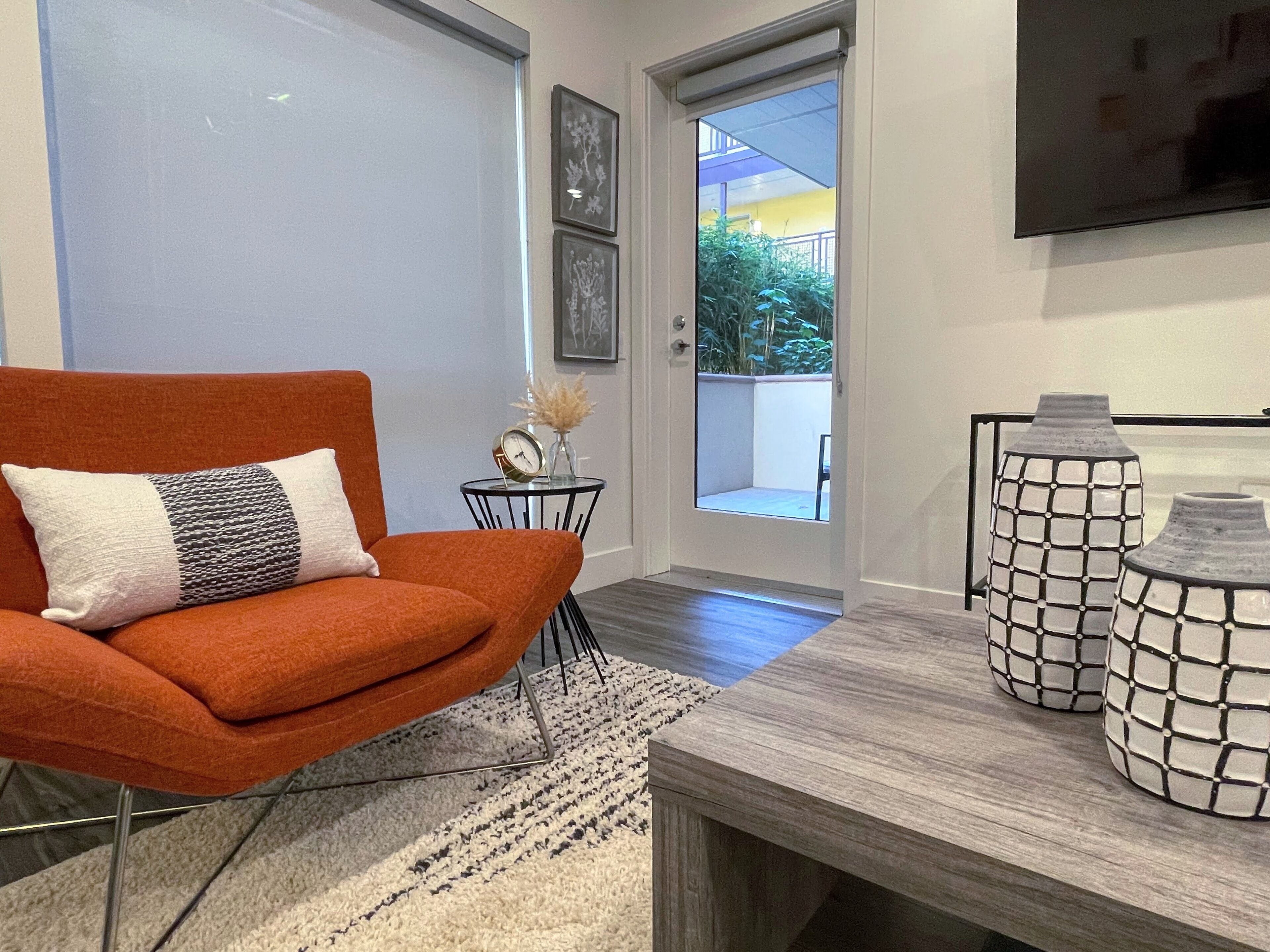 Un salón moderno con un sillón rojo, una mesita de noche con un reloj y un florero, y dos jarrones decorativos sobre una mesa de madera.