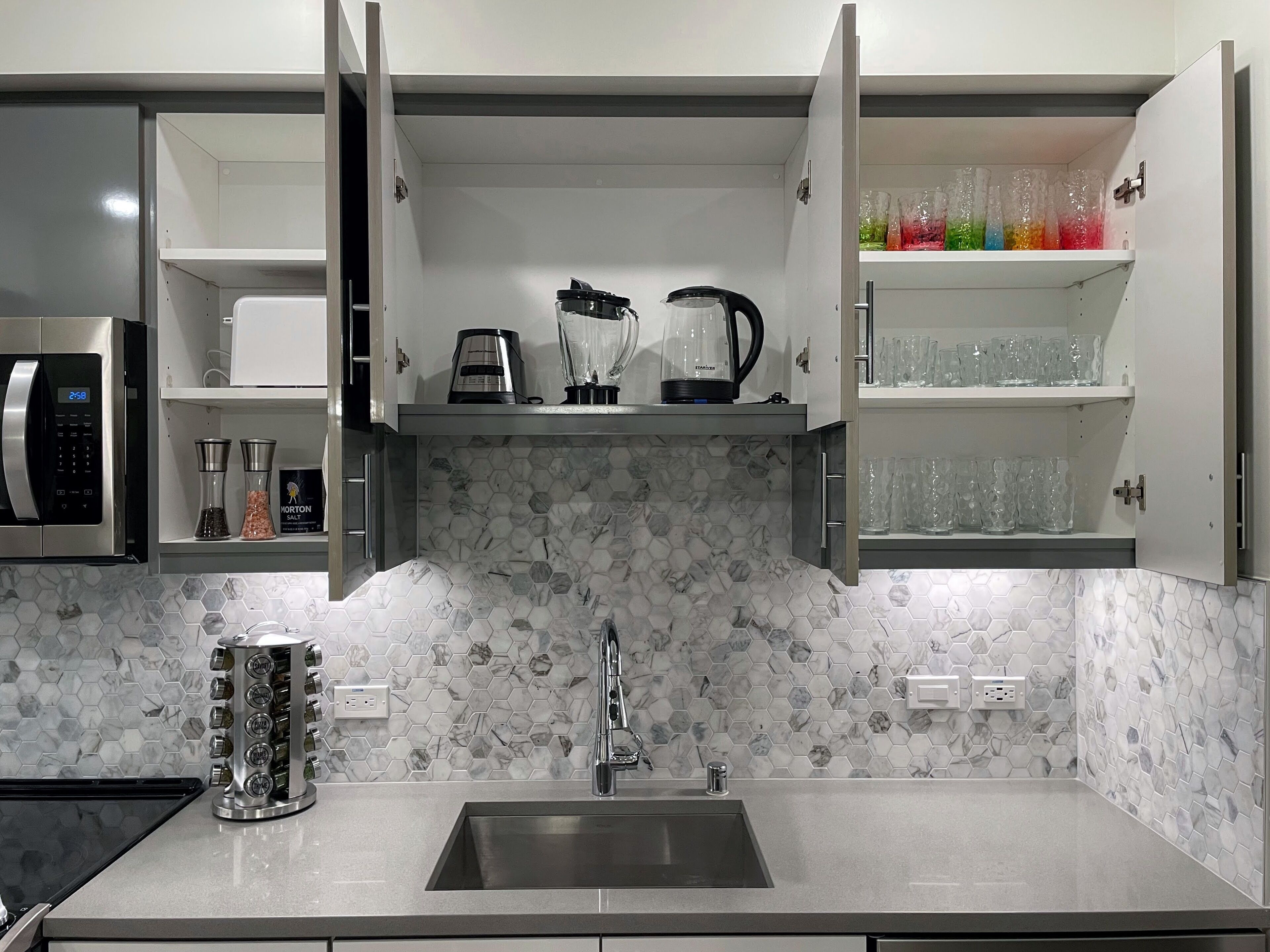 A modern kitchen with a built-in microwave, a coffee maker, a blender, and a kettle on the countertop.
