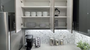 Eine moderne Küche mit offenen Schränken, einer Kaffeemaschine, einer Reibe und einem Blumentopf.